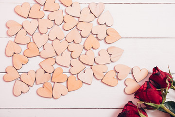Wood hearts and red roses on white wooden background