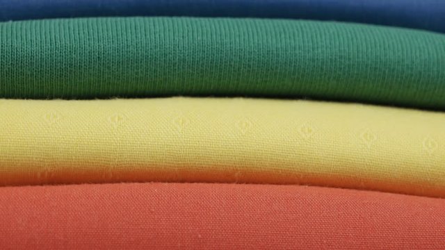 Colorful cotton t-shirts are stacked in a pile in the spectrum of the colors of the rainbow, the background