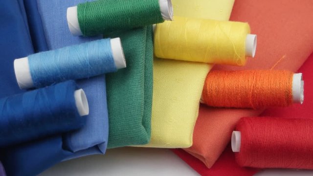 Composition of the set of colorful cotton fabric and spools of colorful thread are stacked in the spectrum of the colors of the rainbow on the white background