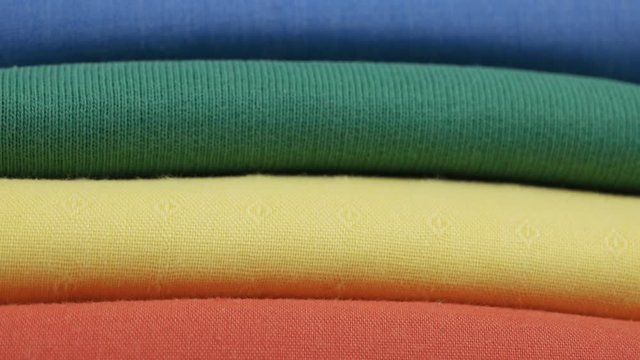 Colorful cotton t-shirts are stacked in a pile in the spectrum of the colors of the rainbow, the background