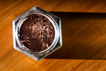 Cocoa powder in glass jar lying on wooden brown table, flat lay view, healthy diet