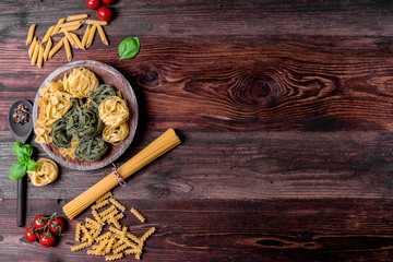 Assortment of many different raw pasta on a rustic board, beautifully arranged with basil and tomatoes