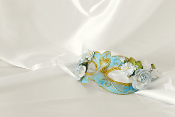 Photo of elegant and delicate light blue venetian mask over white silk background.