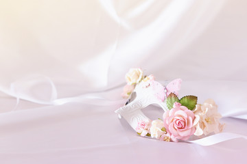 Photo of elegant and delicate white venetian mask with pink floral decorations over silk background.