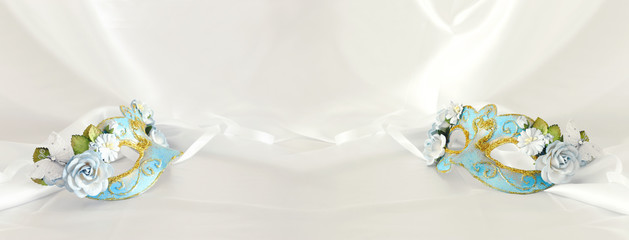 Banner of elegant and delicate light blue venetian mask over white silk background.
