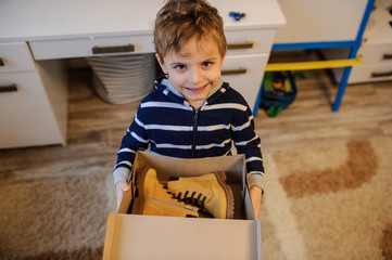 close up of a boy holding a open cardboard box with a pair of yellow leatrher boots