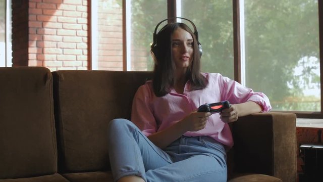 Young female with headphones playing video game using joystick
