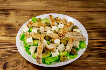 Tasty salad with fried chicken breast, green olives, feta cheese, avocado, lettuce and olive oil on wooden table