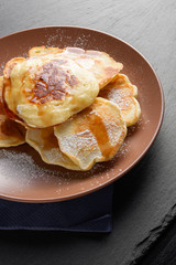 Homemade pancakes with golden syrup and sugar powder on brown plate over a stone plate