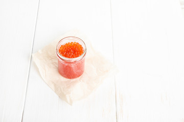 Red caviar in glass bowl on white wooden background