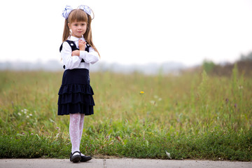 Full-length portrait of cute adorable serious thoughtful first grader girl in school uniform and...