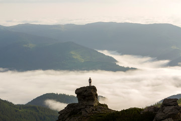 Silhouette of athletic climber tourist on high rocky formation on mountain valley filled with white...