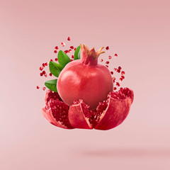 Flying in air fresh ripe whole and cut pomegranate with seeds and leaves