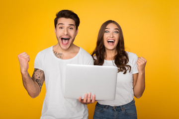 Excited couple screaming and holding laptop on background