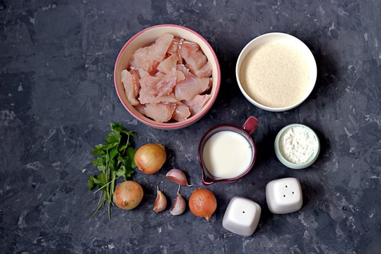 Ingredients for cooking homemade fish cakes: raw fish fillet, onion, garlic, milk, cornstarch, salt, pepper, breadcrumbs, parsley. Top view.