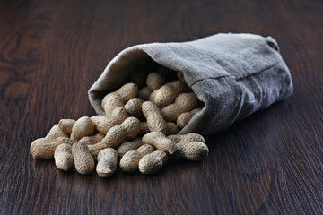 Peanuts in burlap sack on wooden background