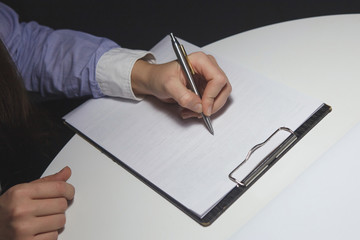 On the table in the night office, a female hand holds a pen on the tablet.