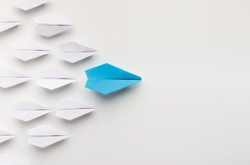 One blue paper plane leading group of white ones