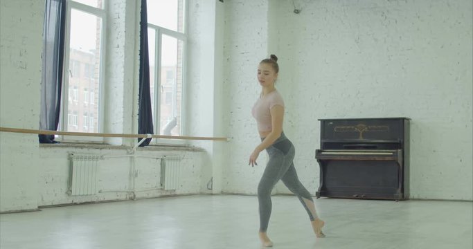 Graceful classic ballet dancer in sportswear practicing fouette exercise in dance studio during rehearsal. Elegant young ballerrina performing elements of classical dance in ballet studio.