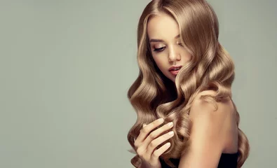 Photo sur Plexiglas Salon de coiffure fille blonde aux cheveux ondulés longs et brillants. Beau modèle de femme souriante avec une coiffure frisée.