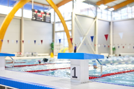 Image of swimming pool with starting blocks and people swimming in the background