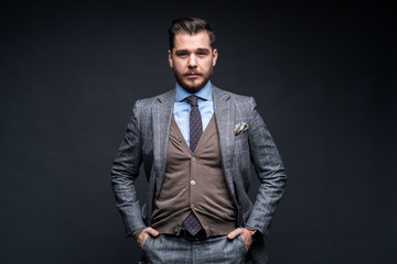 A confident elegant handsome young man standing in front of a black background in a studio wearing a nice suit.