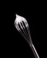 Metal whisk with whipped egg whites, isolated on black background. Clipping path.