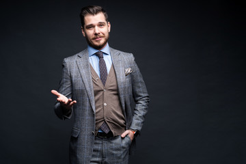 A confident elegant handsome young man standing in front of a black background in a studio wearing...