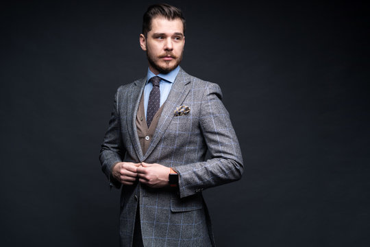 A confident elegant handsome young man standing in front of a black background in a studio wearing a nice suit.