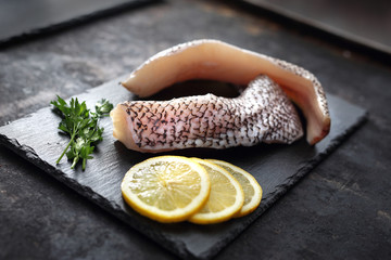 Grenadier na kamiennym talerzu. Surowa ryba na czarnym kamieniu i ciemnym tle. © foodandcook