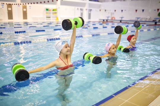 Group of healthy girls doing exercises with dumbbells in the water in indoor swimming pool