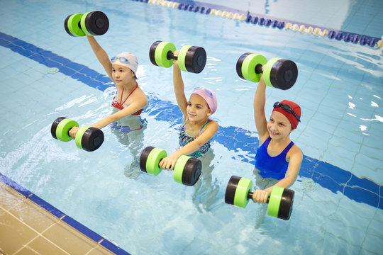 Group of little girls standing in the pool and exercising with dumbbells during aqua aerobics