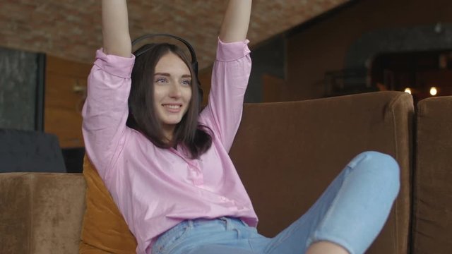 Woman with headphones is sitting on sofa and playing video game
