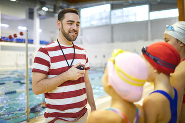 Young swim instructor standing with stopwatch and explaining children the rules of conduct in the pool - Powered by Adobe