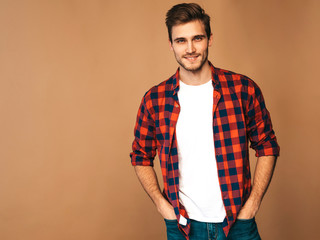 Portrait of handsome smiling stylish hipster lumbersexual businessman model dressed in red checkered shirt. Fashion man posing on golden background