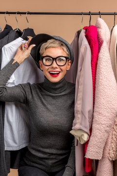 emotional pretty girl is wearing a cap, a sweater and trousers and standing among clothes in the shop . collection of trendy outfits. pretty blond gorl enjoys shopping