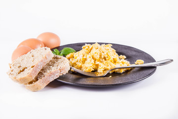 Scrambled eggs, some fresh eggs and wholemeal bread, and a fork, decorated with basil, on a white background 