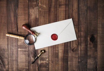 Blank paper envelope with red wax seal, stamp, spoon and magnifier on wooden background. Mockup for...