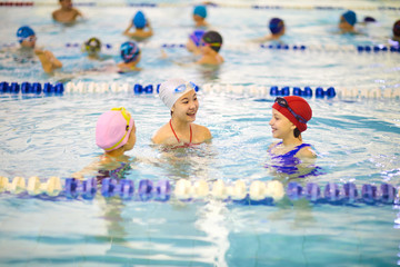 Group of little girls in swimwear swimming together in indoor swimming pool at the leisure center