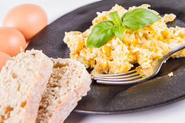 Scrambled eggs, some fresh eggs and wholemeal bread, and a fork, decorated with basil, on a white background 