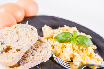 Scrambled eggs, some fresh eggs and wholemeal bread, and a fork, decorated with basil, on a white background 