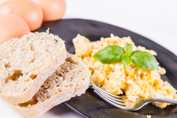 Scrambled eggs, some fresh eggs and wholemeal bread, and a fork, decorated with basil, on a white background 
