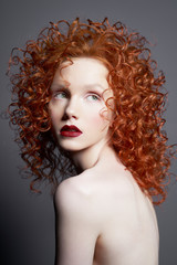 Beautiful young woman with red-hair on grey background. Nude pretty lady with bright red lipsstick and modern art makeup. Sensual model pose in photo-studio. Sexy naked body.