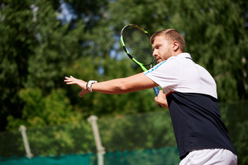 Tennis male player. Handsome bearded sportsman standing with racket in ready stance to receive ball, while playing tennis. Dressed in black and white sportswear.