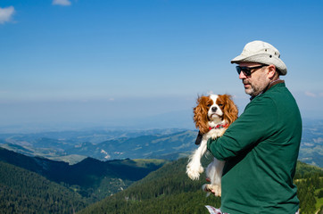 Man holding his dog - Cavalier King Charles Spaniel - in a mountain landscape