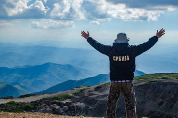 Man with spread arms in a joyful pose, watching an idyllic landscape of the mountain Kopaonik, in Serbia. Translation of the text on the jacket: 