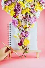 Woman's hands holding brush and drawing on easel with flowers, spring or creativity concept
