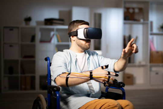 Modern young man with vr goggle and sensors pointing at object or touching display during virtual experience