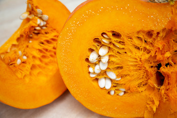 Tasty, healthy and fleshy vegetable - juicy, bright orange pumpkin in a cut with seeds in close-up, next to a cut slice. Pumpkin oval-shaped with a hard crust.