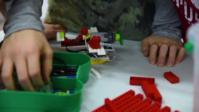 Group of kids building robot constructor from the plastics details programmed on the computer, at robotics school lesson. Education, children, technology, science and futuristic concept. E-learning. 